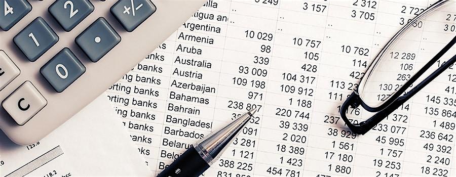 Calculator, pen, and reading glasses atop a financial spreadsheet with country names and numeric data.